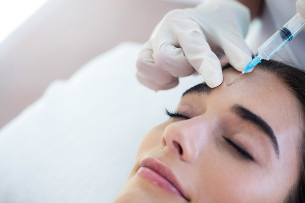 Woman receiving botox via needle in forehead